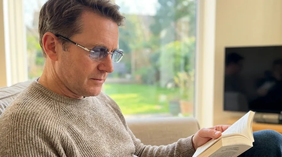Man reading a book on a sofa wearing BlueLume Glasses, from the maker's page